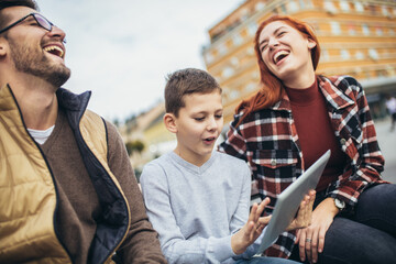 Family sitting on bench, relaxing using gadget, browsing internet.