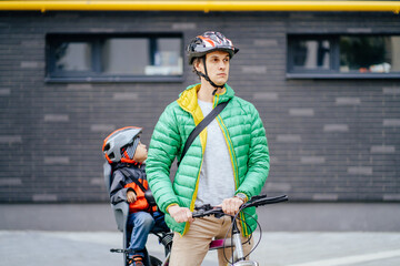 Portrait of little boy with security helmet on the head sitting in bike seat and his father with bicycle on looking forward. Safe and child protection concept.