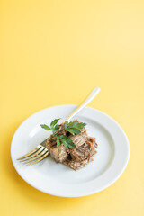 Canned beef stew on white plate with parsley leaf, yellow background