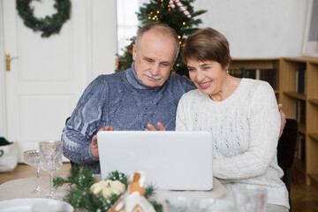 Elderly couple using laptop and having video call with friends or relatives at home. Christmas at home