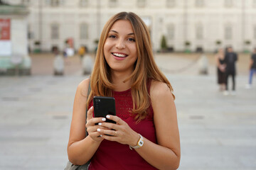 Young pretty woman with long hair looks at the camera holding a mobile phone