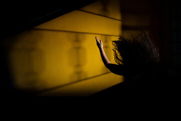 Silhueta de mulher misteriosa com braço pra cima e cabelos esvoaçantes com sombra de uma janela.
