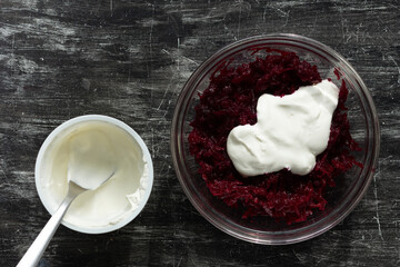 Top view of grated cooked beet in glass bowl and sour cream as ingredients for salad