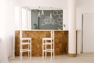 A stylish modern bar counter decorated with wooden tiles and two white bar stools in the living room of the house. Scandinavian interior design