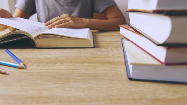Close up and candid 4K of working woman who is reading a book concentratively on table with stacks of books as foreground shows concept of learning knowledge from self studying lifestyle. 