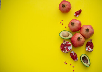 Four juicy and ripe pomegranates and cut cavocado  on yellow background. Fruits contain many vitamins. Fresh fruits:  good for body. food for diet. top view.  place for text