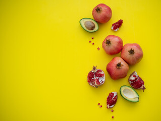 Four juicy and ripe pomegranates and cut cavocado  on yellow background. Fruits contain many vitamins. healthy fruits:  good for body. food for diet. top view.  place for text