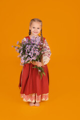 a beautiful little blonde girl in a beige red sundress holds autumn purple flowers on a yellow background