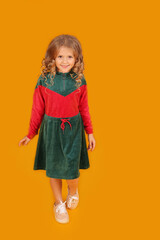 beautiful little blonde girl in a velour red and green dress on a yellow background