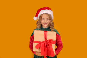 a beautiful blonde girl in a red and green Santa Claus hat dress holds a gift box on a yellow background