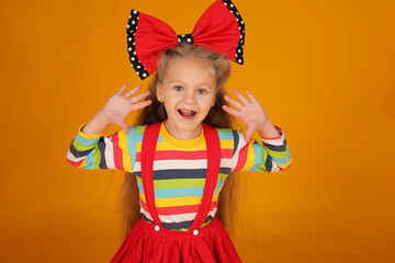 a little happy beautiful blonde girl with long hair with a red bow on her head in a colored jacket on a yellow background