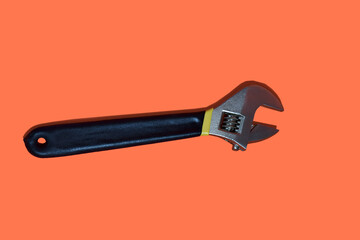 Steel spanner with black handle isolated on red background.