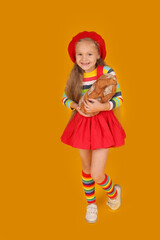 a little happy beautiful blonde girl with long hair in a red beret on her head in a colored jacket in a red skirt on a yellow background holding bread in her hands