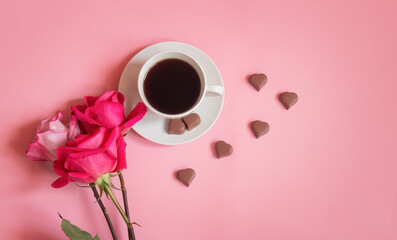 Cup of coffee, heart shape chocolate candies and pink roses.
