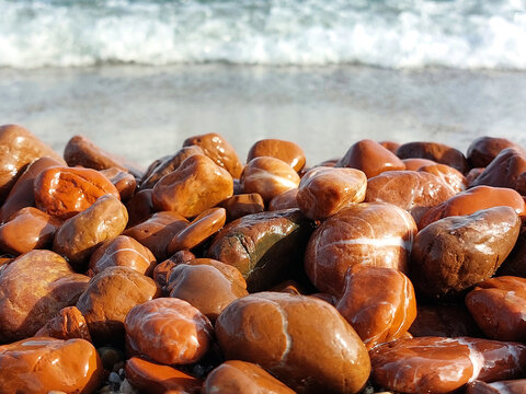 Unique red jasper beach. Many pieces of red jasper polished by the sea. Wet sea stones on a blurred background of the oncoming wave.