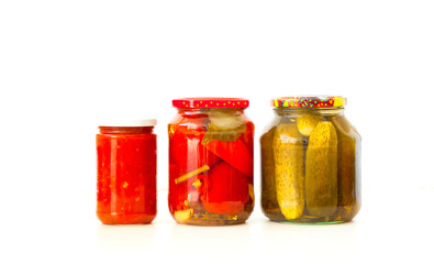 Preserved cucumbers and tomatoes in glass jars on white background. Preparation of products for long-term storage. Close-up