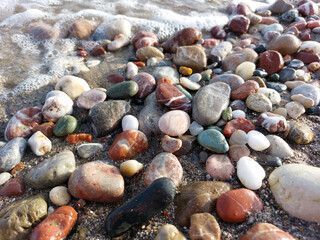 Multicolored sea pebbles close-up in the oncoming wave
