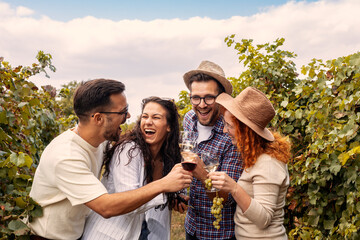Group of four friends smile in vineyard with glasses on hands and grapes