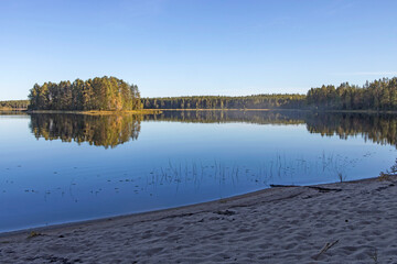 An island overgrown with trees on Lake Onega in Karelia in autumn. Reflections in water