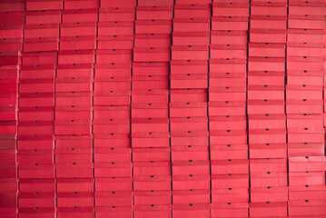 Background of multiple red cardboard package boxes with footwear stacked at a shoe factory warehouse. Shoe manufacturing industry, bulk trade, distribution and business concepts
