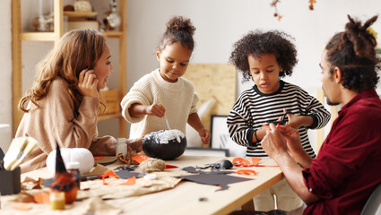 Young joyful african american family mother, father and two kids preparing for Halloween at home