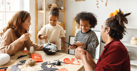 Young joyful african american family mother, father and two kids preparing for Halloween at home