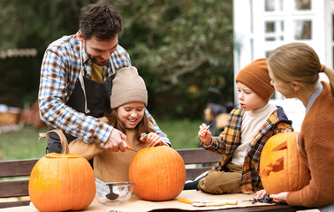 Happy young family carving pumpkins in backyard, children making jack-o-lantern with parents