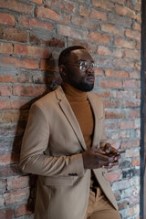 Obraz premium Young serious businessman with smartphone waiting for someone against brick wall