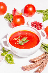 Bowls with homemade tomato soup. Ripe vegetables, fresh basil leaves, breadsticks, aromatic spices