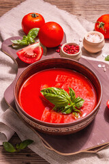 Tomato soup with basil in a bowl. Ripe vegetables, fresh greens, fragrant spices. Vintage wooden table, close up