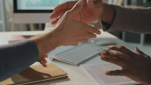 Horizontal slow motion shot footage of unrecognizable multi-ethnic managers sitting in front of each other making agreement and shaking hands