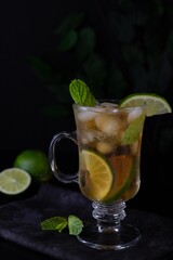 Iced cocktail with lime, mint and ice cubes in glass on the table. Vertical with copy space