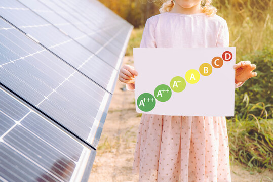 Energy Consumption Labeling Scheme. Solar Power And Energy Efficiency Concept. Girl Child Standing Next To Home Solar Farm With Help Reduce Electricity Cost.