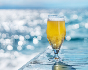 Cooled glass of beer on the blue wooden table. Blurred sea is at the background.