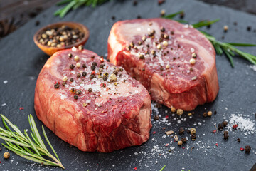Raw Ribeye steaks with salt and herbs on grey board. Top view.