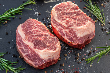 Raw Ribeye steaks with salt and herbs on grey board. Top view.