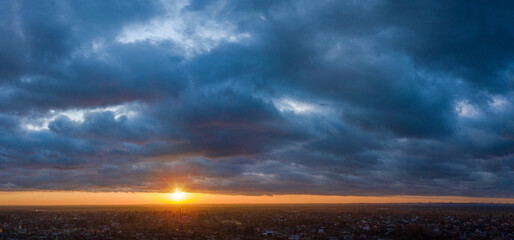 Colorful sunset and red sun in the heavy cloudy sky above the village. Beautiful nature background.