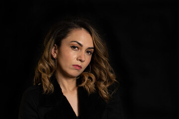 Fototapeta premium Dramatic portrait of a Latina woman with serious or arrogant expression looking straight into the camera over black background