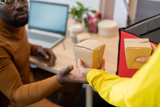 Hand of African businessman taking box with ordered chinese wok held by courier