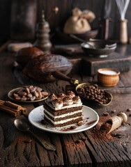 Slice of chocolate cake with tiramisu cream and cocoa powder on wooden table.