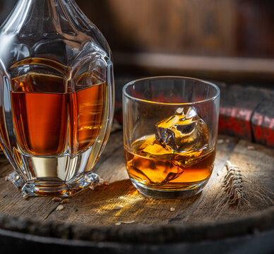 Carafe of whisky and glass of whisky on old wooden cask at the dark background.