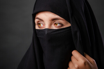 Naklejka premium Close up portrait of young, adult woman in black burqa with hidden face, isolated on black background.