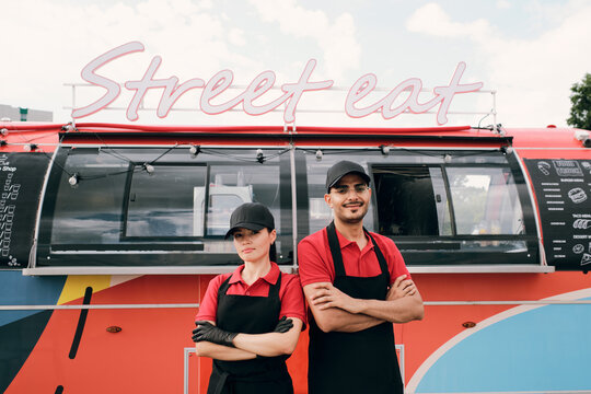Two young successful colleagues in uniform standing against street food truck - Powered by Adobe