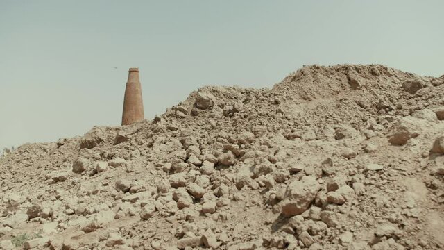 A brick factory in Pakistan that uses slave labor. On the sand there is an empty trailer. Big brick pipe with smoke on background. Slow motion