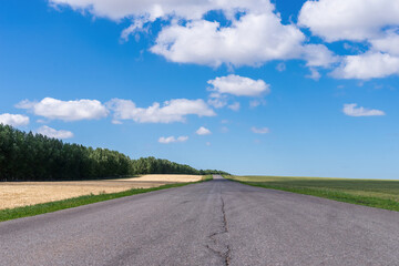Paved road in the field and clouds in the blue sky.