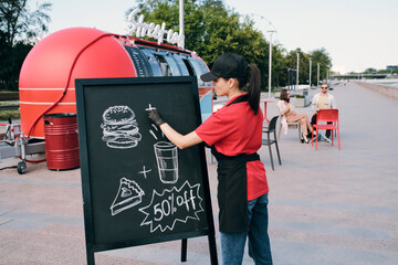Young businesswoman drawing picture of fast food and drink on discount on blackboard