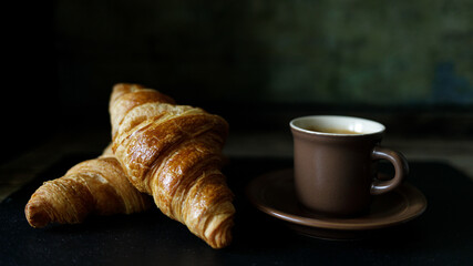 Cup of hot coffee with two fresh croissants against dark background