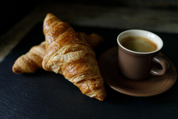 Cup of hot coffee with two fresh croissants against dark background