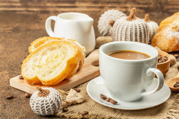 Breakfast concept with a cup of coffee, croissants, milk jug, and decorative crochet pumpkins