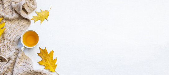 Minimalism style autumn composition with cup of herbal tea, dry leaves and warm blanket on white marble background top view. Long banner format.